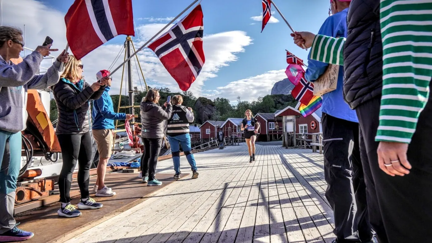 Supportere med flagg heier fram en løper på brygga under Lofotstafetten