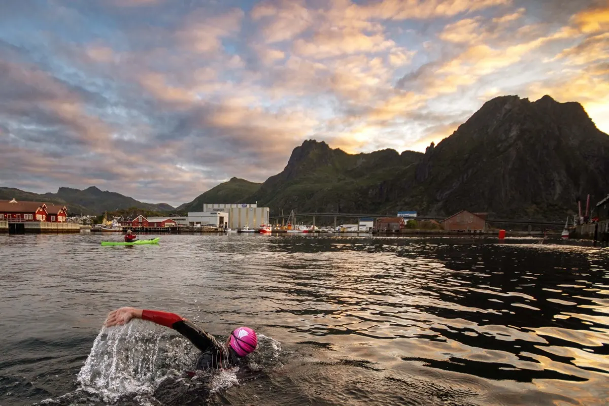 Swimmer in Svolvaer harbour at sunrise, kayak alongside and the peaks behind